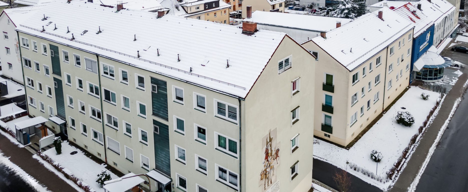 Ansicht Wohnblock von oben, 4 Stockwerke, 2 Eingänge, auf Seitenwand eine Malerei zu sehen. Es liegt Schnee.
