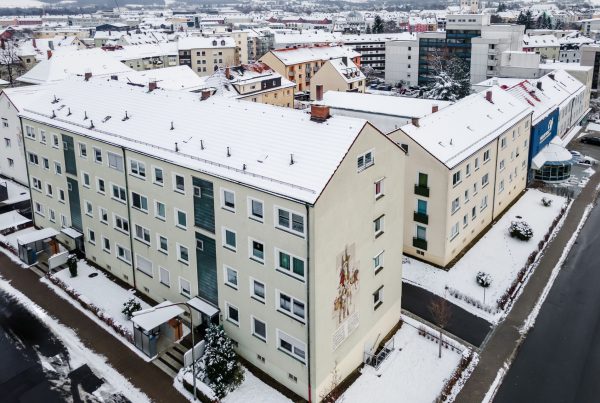 Ansicht Wohnblock von oben, 4 Stockwerke, 2 Eingänge, auf Seitenwand eine Malerei zu sehen. Es liegt Schnee.