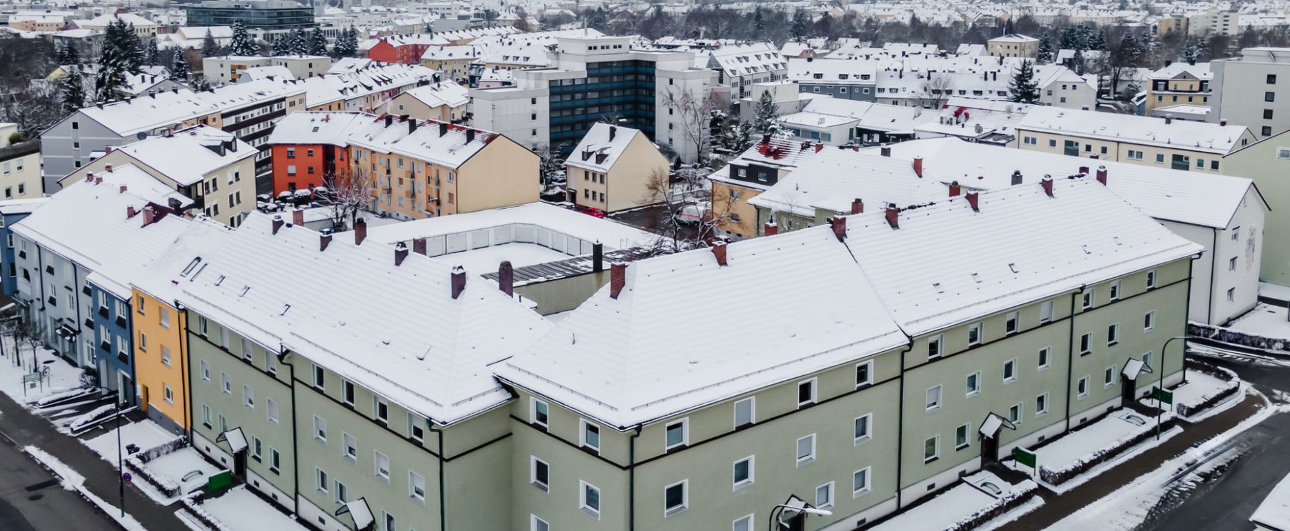 Ansicht Wohnblock aus Vogelperspektive, grüne Fassade, 3 Stockwerke mit 5 Eingänge.